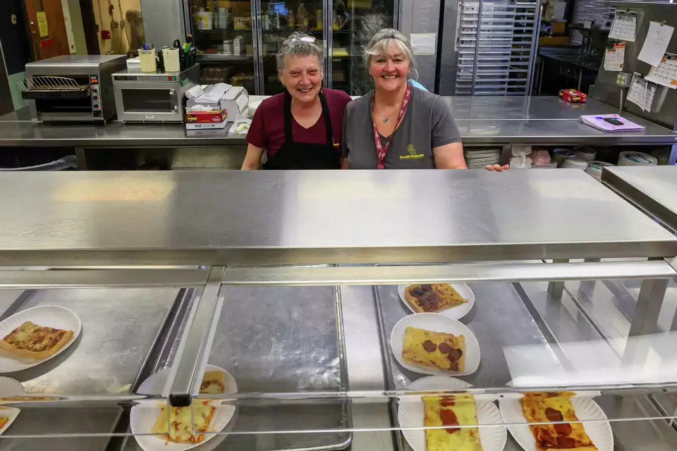 two cafeteria workers smiling in the school cafeteria kitchen
