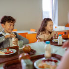 Cheerful boy opening his bottle of milk while having lunch with classmates