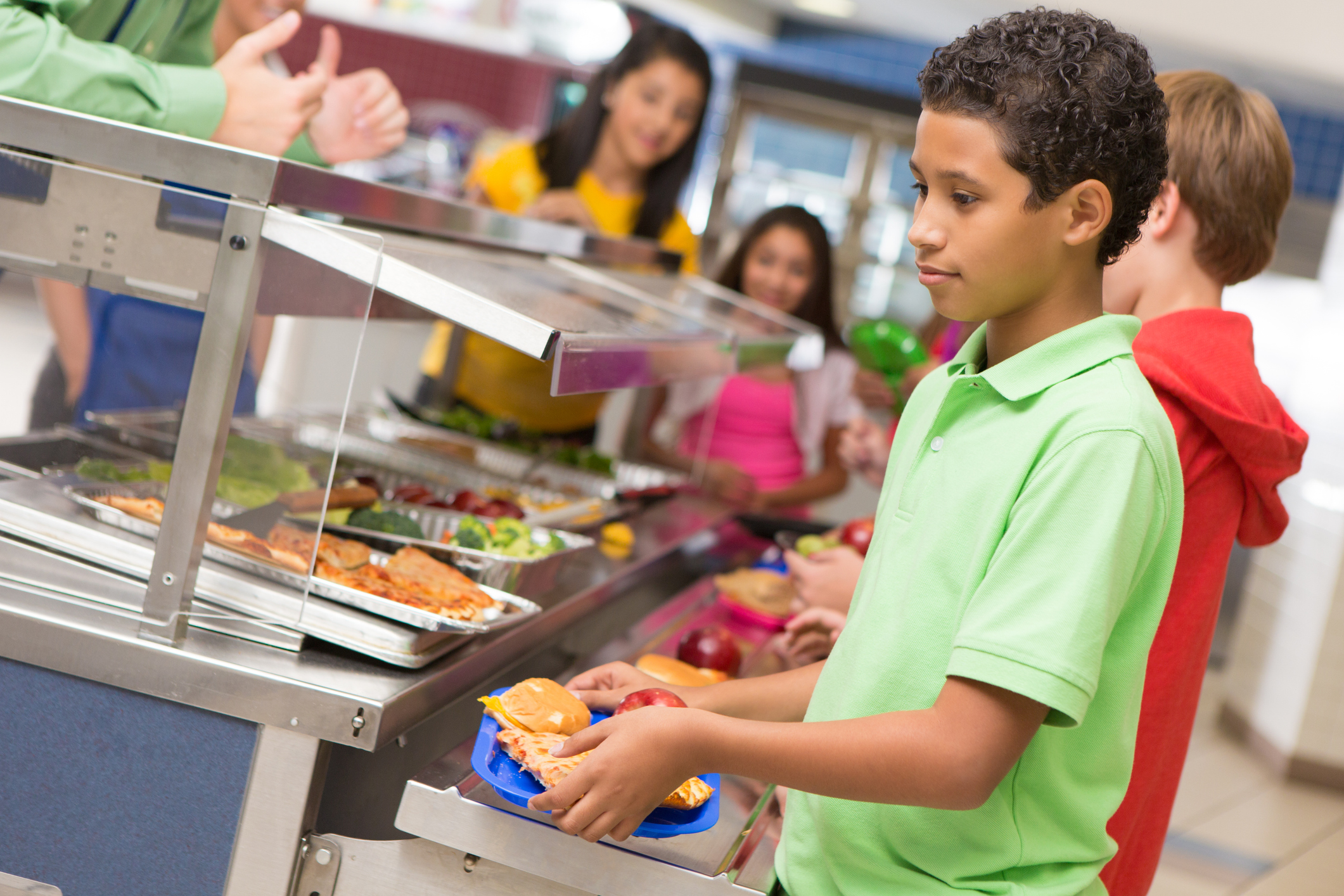 Middle school students getting lunch items in cafeteria line.