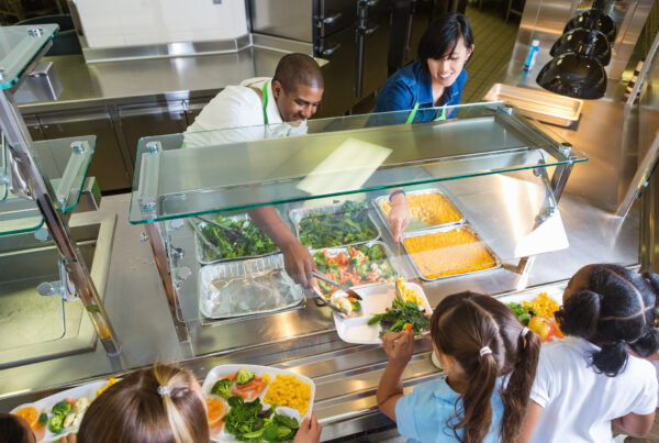 Cafeteria worker serving trays of healthy food to children