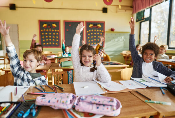 Large group of happy elementary students raising their hands in class